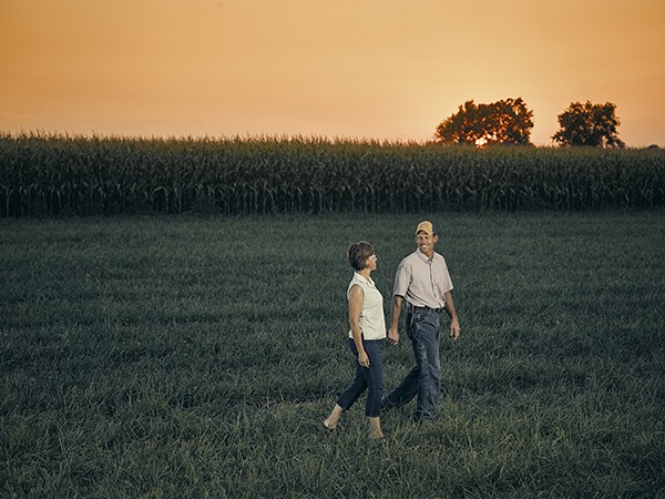 man and woman walking in front of corn field